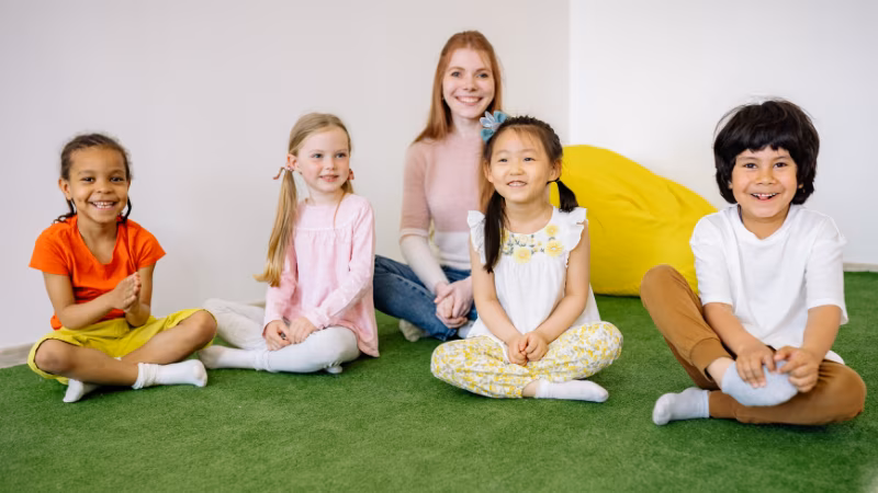 HappyChildrenAndTeacherSittingonGreenGrassCarpet-