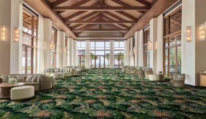 Luxury tropical hospitality interior featuring lush botanical carpet flooring, warm wooden architecture, ocean-view lounge space, and resort-inspired design from Shaw Contract ROAM collection.